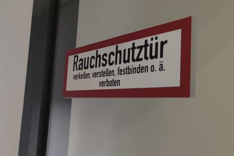 Der Hinweisaufkleber an einer Tür mit dem Hinweis „Rauchschutztür. verkeilen, verstellen, festbinden o. ä. verboten