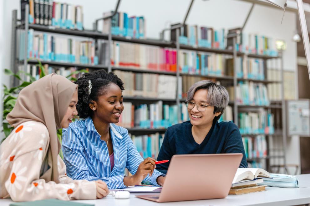 Drei Studentinnen sitzen in der Biblitohek und schauen auf einen Laptop