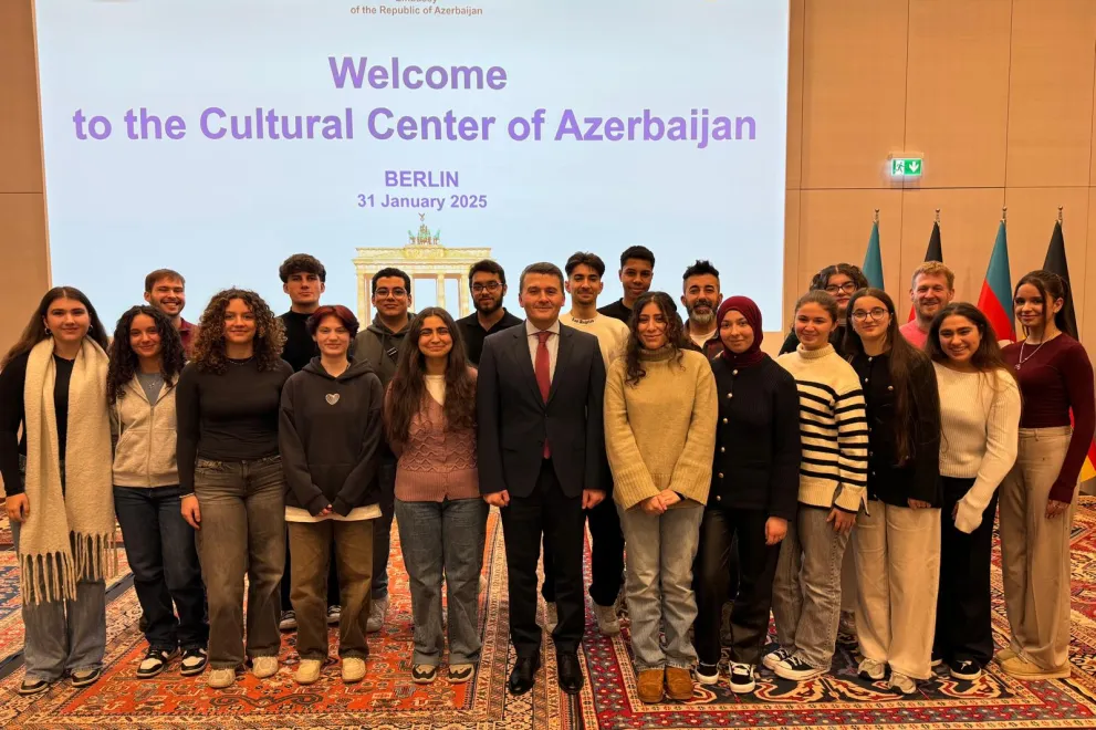 Foto: Gruppe von Schülerinnen und Schülern des TalentKollegs Ruhr Hagen mit dem Botschafter der Republik Aserbaidschan in Deutschland in der Mitte. Im Hintergrund ist eine projizierte Präsentation zu sehen mit dem Titel "Welcome to the Cultural Center of Azerbaijan; Berlin, 31 January 2025".