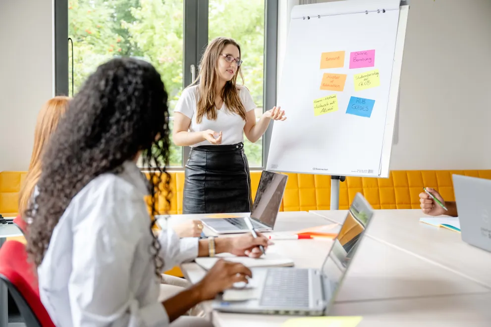Junge Frau steht an Flipchart und erklärt. 