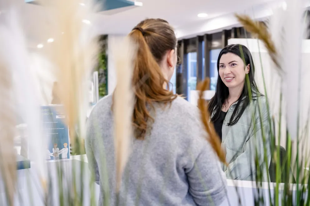 Blick über die Schulter einer Frau auf eine andere junge Frau, die etwas erklärt. 