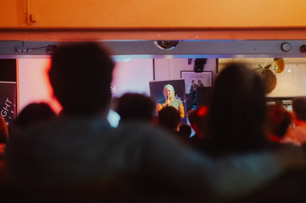 Junge Frau steht auf einer Bühne und erzählt dem Publikum etwas,