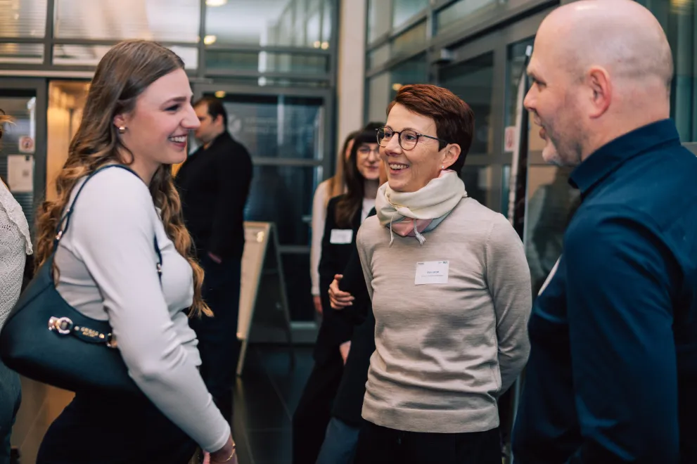 Foto: Drei Personen stehen im Kreis und unterhalten sich. Sie lächeln.