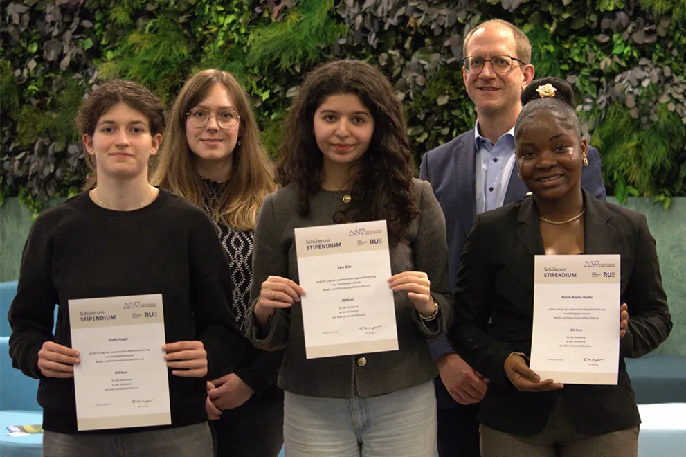 Foto: Gruppenfoto mit mehreren Personen. Drei von ihnen halten Urkunden hoch.