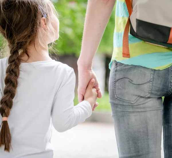 Das Foto zeigt von hinten eine Mutter und ihr Kind, die sich an den Händen halten